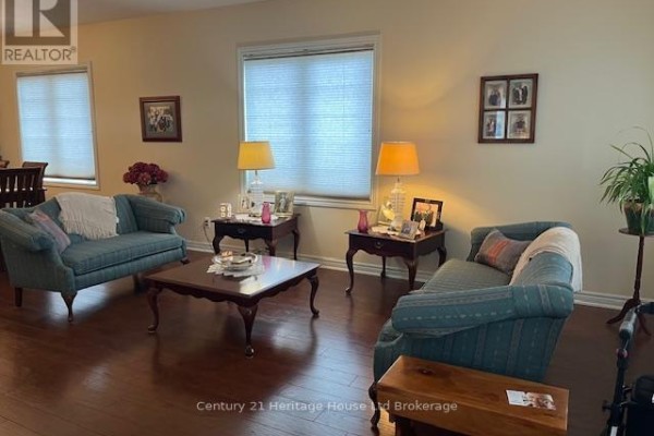 Living room showing two teal sofas, end tables with lamps, and a view into the dining area. - 1 - 21 Balazs Court, Tillsonburg