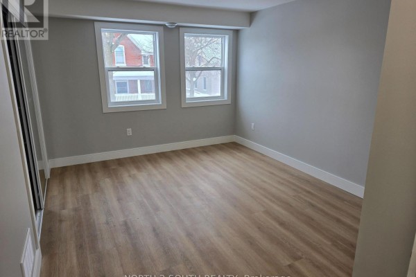 Empty bedroom with light wood floors, two windows, and grey walls. - 1 - 241 Darling Street, Brantford