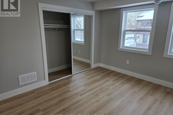 Bedroom with mirrored closet doors, light wood floors, and windows overlooking the exterior. - 1 - 241 Darling Street, Brantford