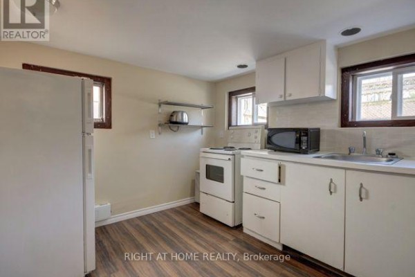 Compact kitchen with white cabinets, white stove, microwave, sink, and beige walls. - 1 - 26 Victoria Street, Toronto