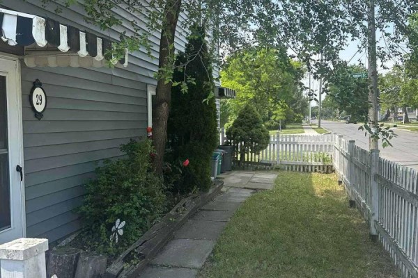 Path to front door with gray siding, white picket fence, and green trees. - 1 - 29 Rykert Street, St  Catharines