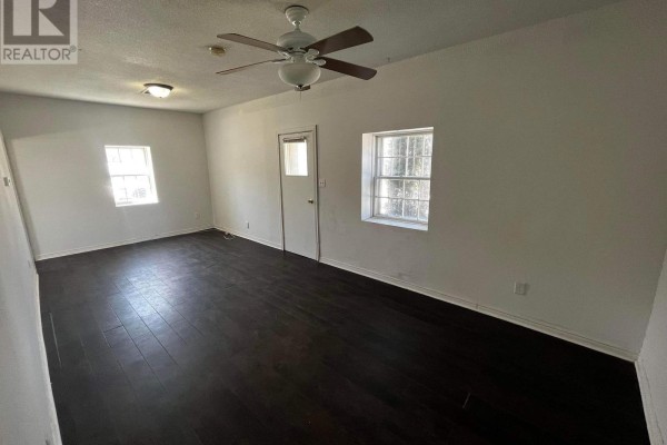 Living room with dark wood floors, white walls, ceiling fan, and two windows. - 1 - 29 Rykert Street, St  Catharines