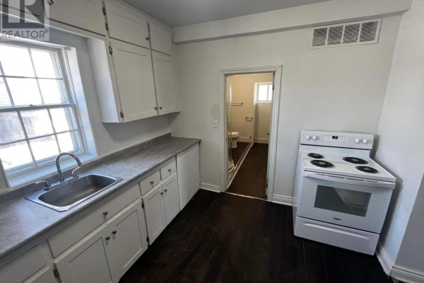 Kitchen with white cabinets, stainless steel sink, and white stove, leading to bathroom. - 1 - 29 Rykert Street, St  Catharines