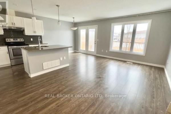 Open concept living area with a kitchen island, dining space, and large windows overlooking a backyard deck. - 1 - 3400 Castle Rock Place, London South