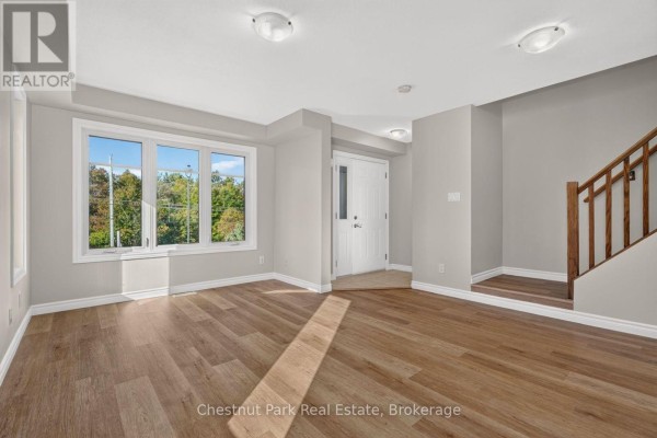 Empty living room with wood floors, large bay window overlooking trees, and front door. - 1 - 37 Silver Street, Huntsville