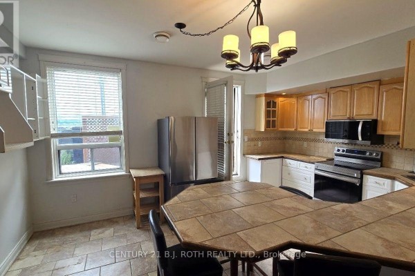 Kitchen with stainless steel refrigerator, island with tiled tabletop, and wood cabinets. - 1 - 41 Dunlop Street E, Barrie