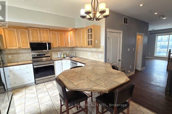 Kitchen with wood cabinets, peninsula counter, and view into adjacent living space. - 1 - 41 Dunlop Street E, Barrie
