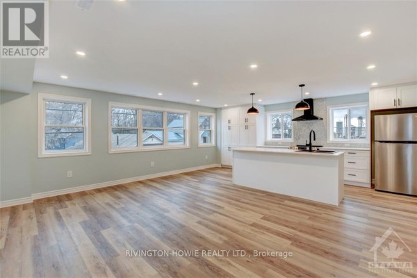 Open-concept living area with a modern white kitchen island, stainless steel appliances, and large windows. - 1 - 413 Donald B Munro Drive, Ottawa