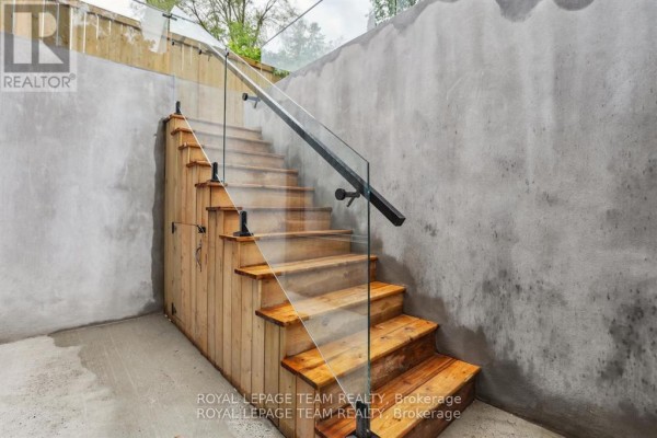 Wooden outdoor staircase with glass railing leading down into a concrete area. - 1 - 47 Grosvenor Avenue, Ottawa