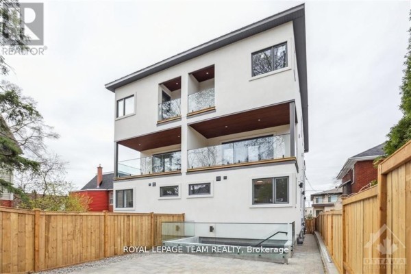 Rear exterior of a three-story white building with multiple balconies and wooden fences. - 1 - 47 Grosvenor Avenue, Ottawa
