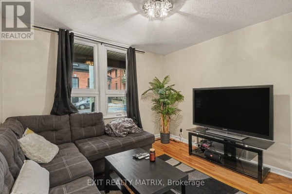 Living room with grey sectional sofa, black coffee table, television, and window view of street. - 1 - 511 Cooper Street, Ottawa