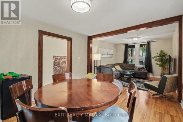 Dining area with round wood table and chairs, opening into living room with sectional sofa. - 1 - 511 Cooper Street, Ottawa