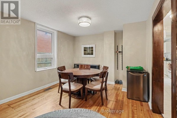 Dining area with round wood table and chairs, window view of brick exterior, and mini fridge. - 1 - 511 Cooper Street, Ottawa