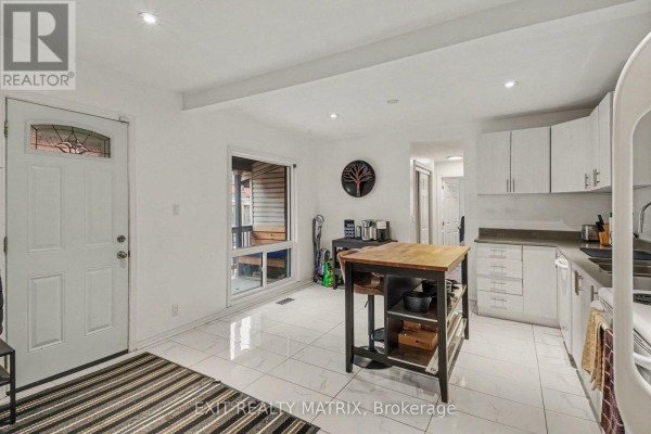Kitchen with white cabinets, butcher block island, and tiled floors with a front door. - 1 - 511 Cooper Street, Ottawa
