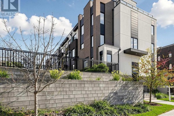 Townhouse building with a tiered brick wall and landscaping in the foreground. - 1 - 55 Thomas Mulholland Drive, Toronto