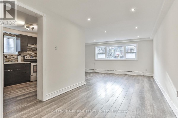 Living area with grey wood floors, white walls, and view into kitchen. - 1 - 76 Walmsley Boulevard, Toronto