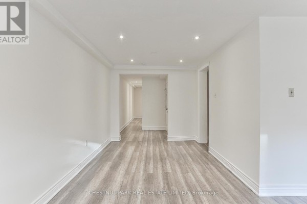 Open white living area with grey wood floors and hallway entrance. - 1 - 76 Walmsley Boulevard, Toronto