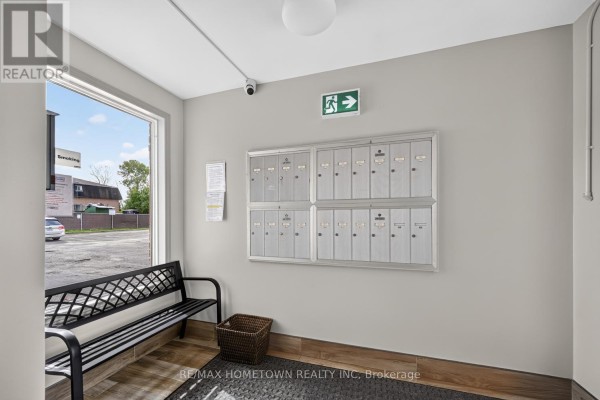 Mailboxes mounted on a grey wall in a building lobby with a bench and window. - 1 - 819 Macodrum Drive, Brockville