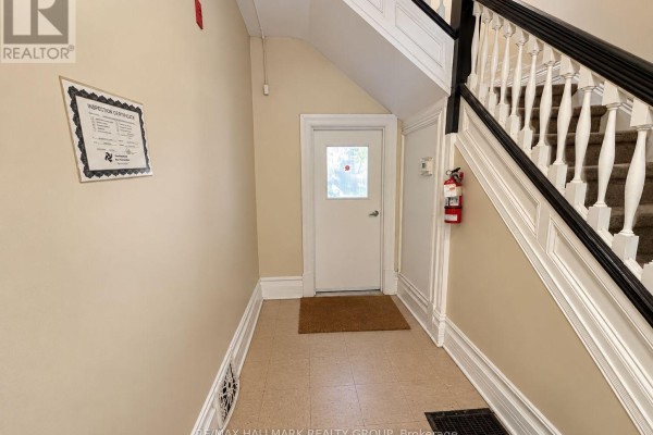Interior hallway with beige walls, a white door, and a staircase with black banister. - 1 - 85 Park Avenue, Ottawa