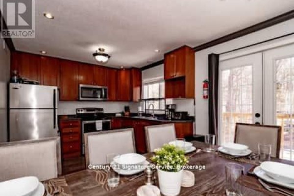 Dining area adjacent to a kitchen with dark wood cabinets, stainless steel appliances, and a patio door. - 1 - 879 Stephenson Road E, Huntsville