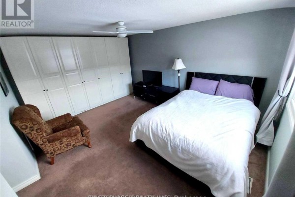 Bedroom with queen bed, armchair, dresser, and large white wardrobe. - #1 - 880 Leslie Valley Drive, Newmarket