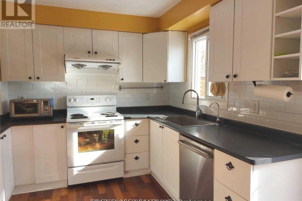 White kitchen with white cabinets, black countertops, white subway tile backsplash, and stainless steel dishwasher. - #1 - 880 Leslie Valley Drive, Newmarket