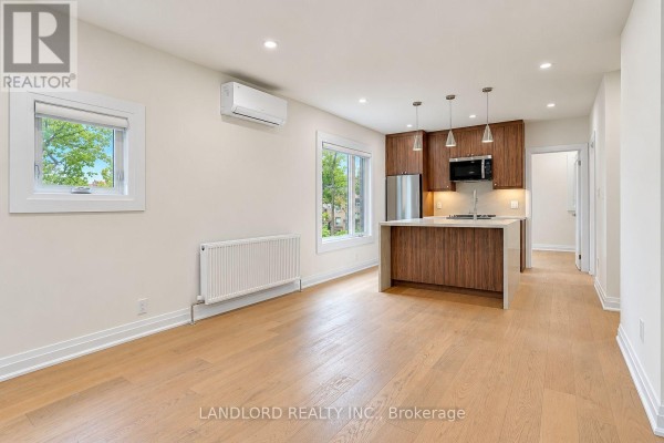 Living room with light wood floors, white walls, and a view of the kitchen. - 1 - 92 Neville Park Boulevard, Toronto