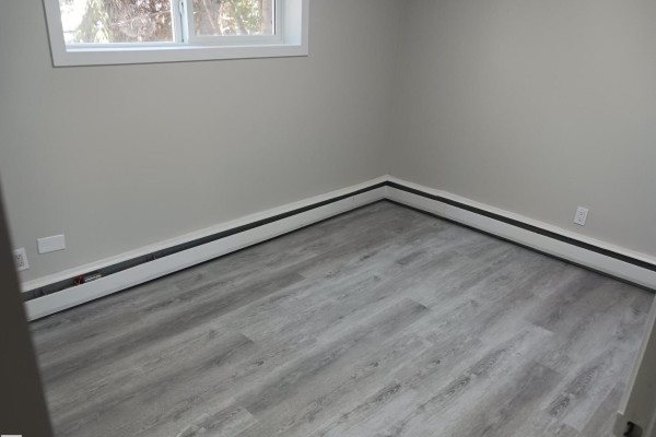Empty bedroom with light grey walls, white baseboard heating, and light wood-look flooring. - #1 10045 154 St Nw, Edmonton