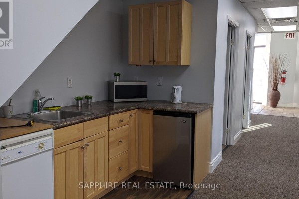 Small kitchenette with light wood cabinets, stainless steel sink, microwave, and mini-fridge. - 1-102 - 7885 Tranmere Drive, Mississauga