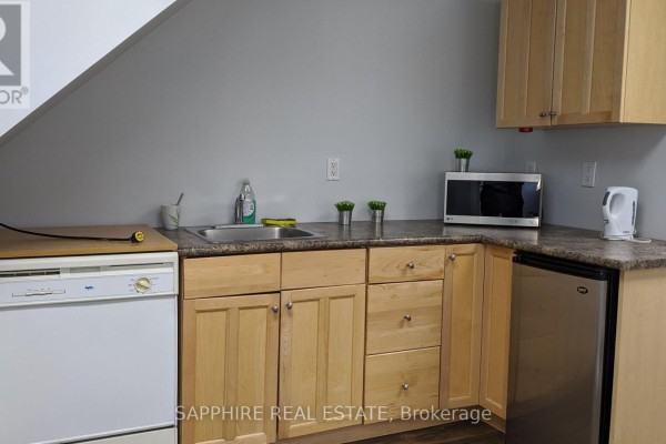 Small kitchenette with light wood cabinets, stainless steel sink, microwave, and mini-fridge. - 1-102 - 7885 Tranmere Drive, Mississauga