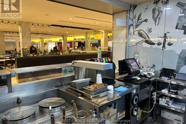 Food service counter with cooking equipment, touch screen ordering stations, and decorative wall art. - 1-134 - 100 City Centre Drive, Mississauga
