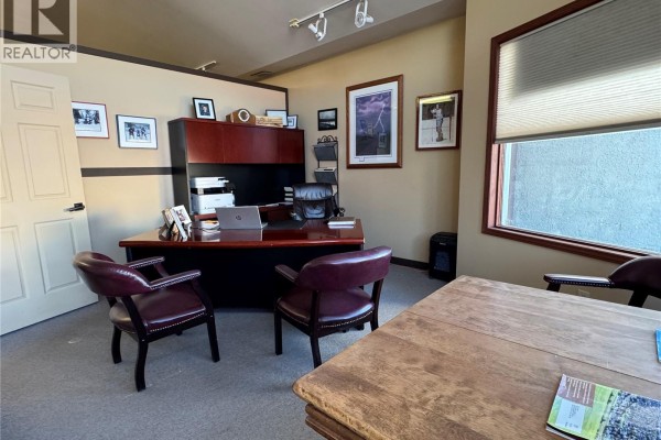 Corner office with a large desk, executive chair, visitor chairs, wooden table, and framed pictures. - 1 181 Broadway Street E, Fort Qu Appelle