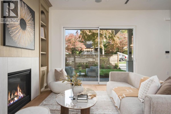Living room with fireplace, sofa, and sliding glass door showing backyard with trees and fence. - 1 2344 W 45th Avenue, Vancouver