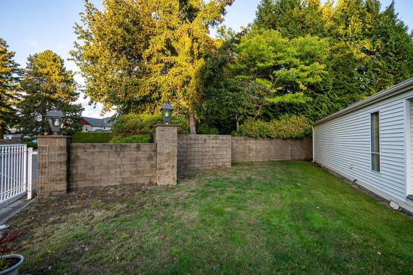Backyard view of a tan block retaining wall with two decorative lampposts and green grass. - 1 2345 Cranley Drive, Surrey