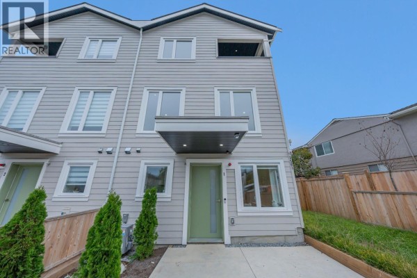 Front exterior of a grey duplex with a green front door and a small paved patio. - 1 3581 Haida Drive, Vancouver