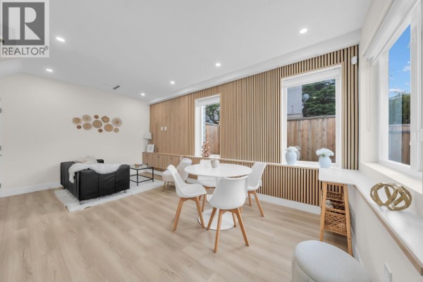 Spacious living and dining area with black couch, white chairs, light wood accents, and windows. - 1 3581 Haida Drive, Vancouver