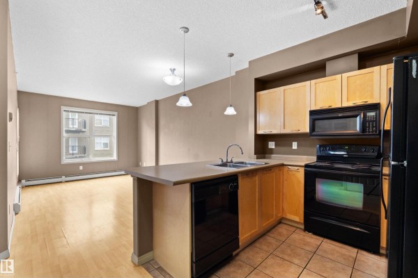 Apartment kitchen with island, light wood cabinets, and view of living area. - #1-516 4245 139 Av Nw, Edmonton