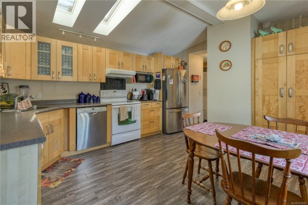 Kitchen with light wood cabinets, stainless steel appliances, and a small dining table. - 1 5250 Beaver Harbour Rd, Port Hardy