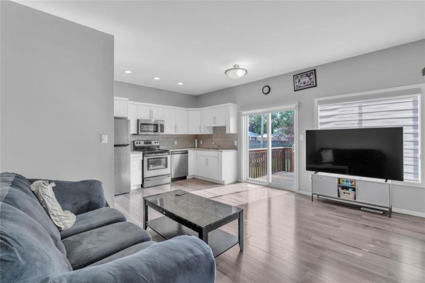Living room and kitchen area with a grey sectional sofa, dark coffee table, and white cabinets. - 1 548 Dufferin Avenue, Selkirk