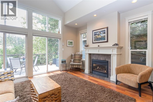 Living room with fireplace, wood floors, large windows, seating, and view of the deck. - 1 551 Bezanton Way, Colwood