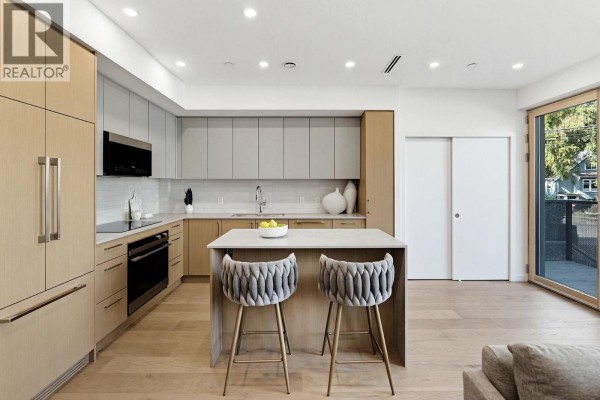 Open-concept kitchen and living area with light wood floors, modern cabinetry, and sliding glass doors leading outside. - 1 60 E 17th Avenue, Vancouver