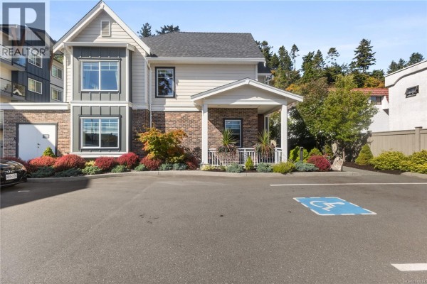 Townhouse exterior with brick and beige siding, covered entrance, and parking lot with accessible spot. - 1 796 Island Hwy S, Campbell River