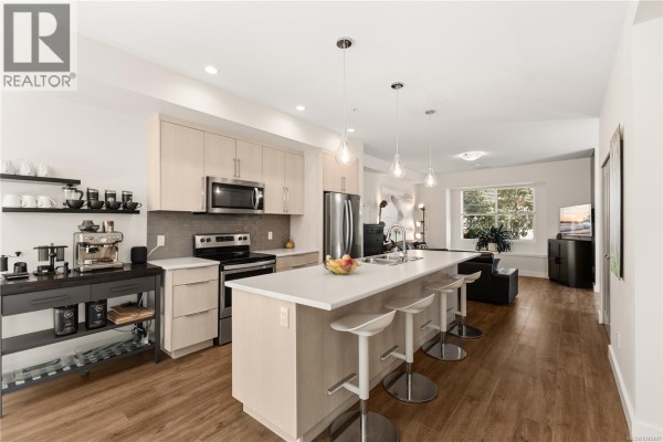 Modern kitchen with light wood cabinets, white island with pendant lights, stainless steel appliances. - 1 796 Island Hwy S, Campbell River