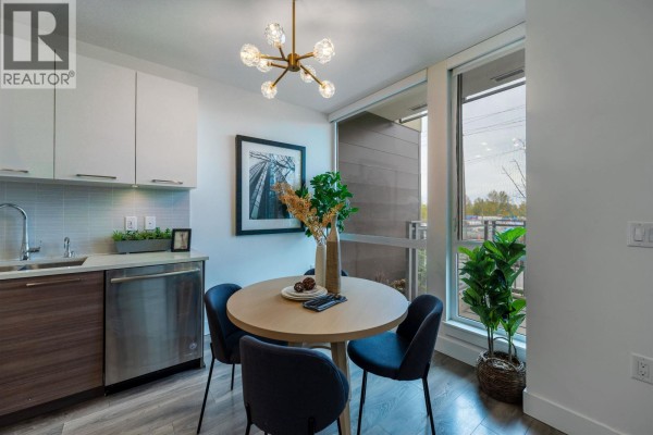 Compact dining area with a round table, chairs, and a small kitchen. - 1 8599 River District Crossing, Vancouver