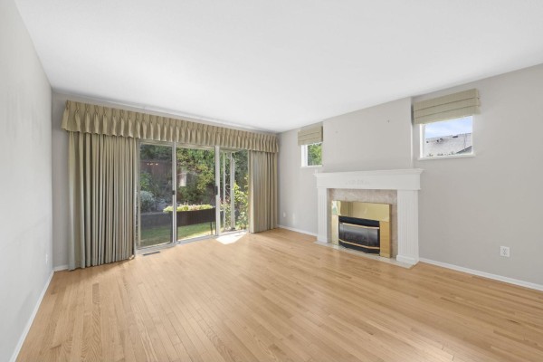 Living room with fireplace, wood floors, sofa, armchair, and large sliding glass doors. - 1 8889 212 Street, Langley