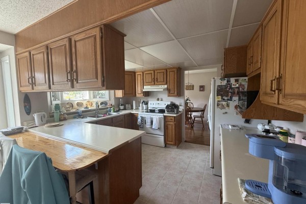 Spacious kitchen with light tiled floors, oak cabinets, a double sink, a stove, and a view to a dining area. - 1 Adamic Cr, Leduc