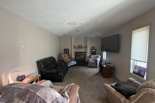 Living room featuring a fireplace, black leather sofa, recliner chairs, a mounted TV, and carpeted flooring. - 1 Adamic Cr, Leduc