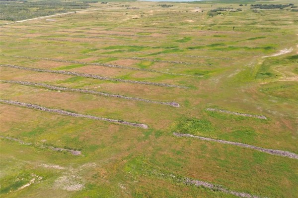 Aerial view of a curving gravel road alongside green fields with rows of debris and distant trees. - 1 Cayer Road, Ste Rose Du Lac