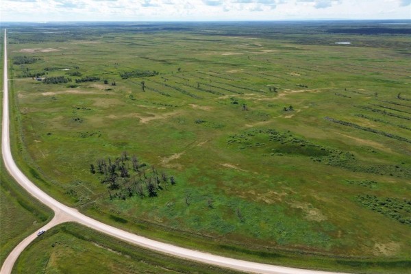 Aerial view of cleared land with rows of debris, a small pond, and a gravel road leading to a building. - 1 Cayer Road, Ste Rose Du Lac