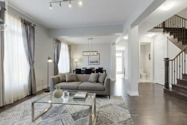 Living room with sofa and coffee table, open to dining area and kitchen with dark cabinets. - 1 Citrine Drive, Bradford West Gwillimbury